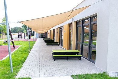 Auf der Terrasse stehen Bänkchen mit leuchtend grünen Sitzflächen, über die mehrere Sonnensegel gespannt sind.